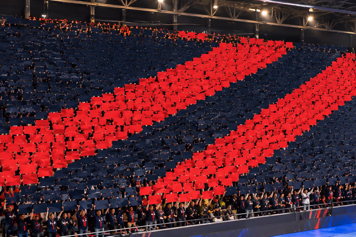 Mosaico de papel en la grada de un pabellón: miles de hojas rojas y azules forman dos franjas diagonales