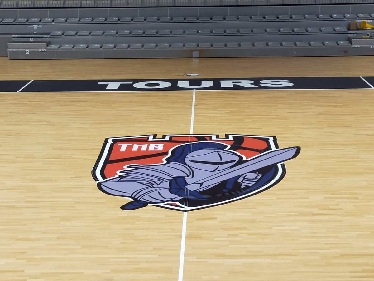 Vinilo de círculo central en el parquet de un pabellón de baloncesto con gradas retráctiles al fondo