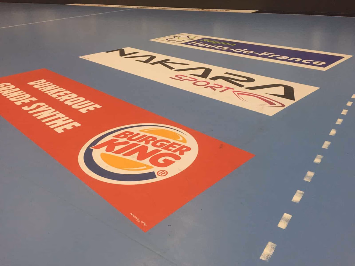Vinilo de círculo central en el parquet de una pista de fútbol sala, con gradas al fondo